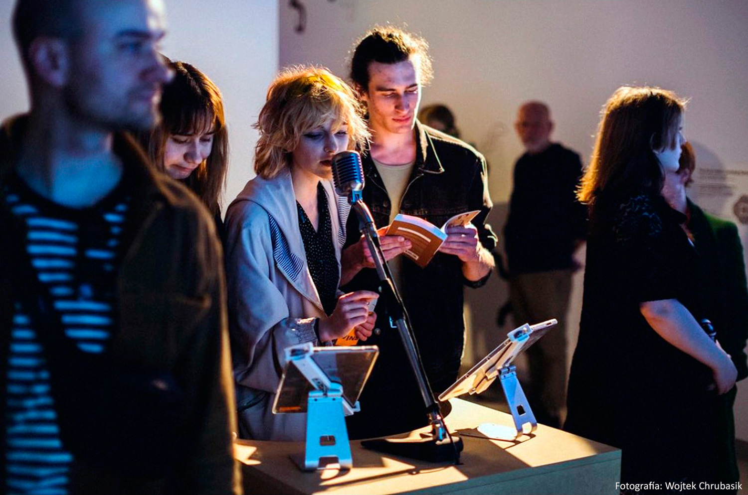 Una chica hablando por un micrófono y un chico leyendo un libro en una exposición