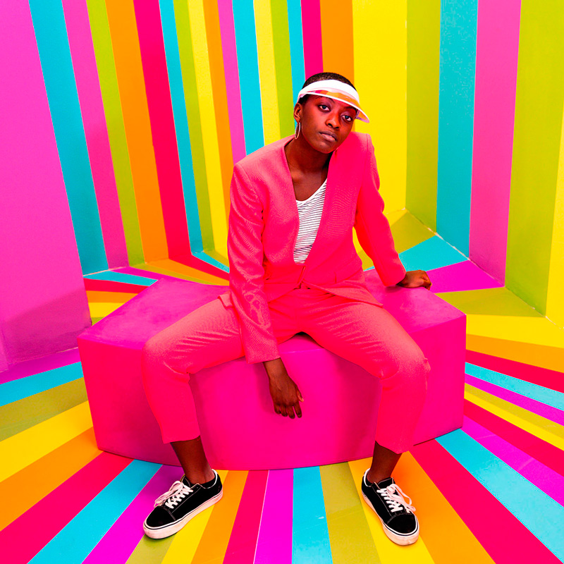 Mujer sentada con vestido rosa en habitación color arcoíris psicodélico